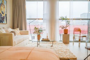Una sala de estar moderna con un sofá, una mesa de centro de vidrio y vistas de la ciudad a través de amplios ventanales.