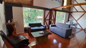 A room with a wooden floor, a sofa, a coffee table, and a view of greenery outside. - Cozy Lodging in the coffee growing region (Ulloa)