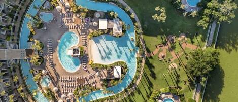 Vista aérea de un resort con múltiples piscinas, tumbonas y un césped bien cuidado.
