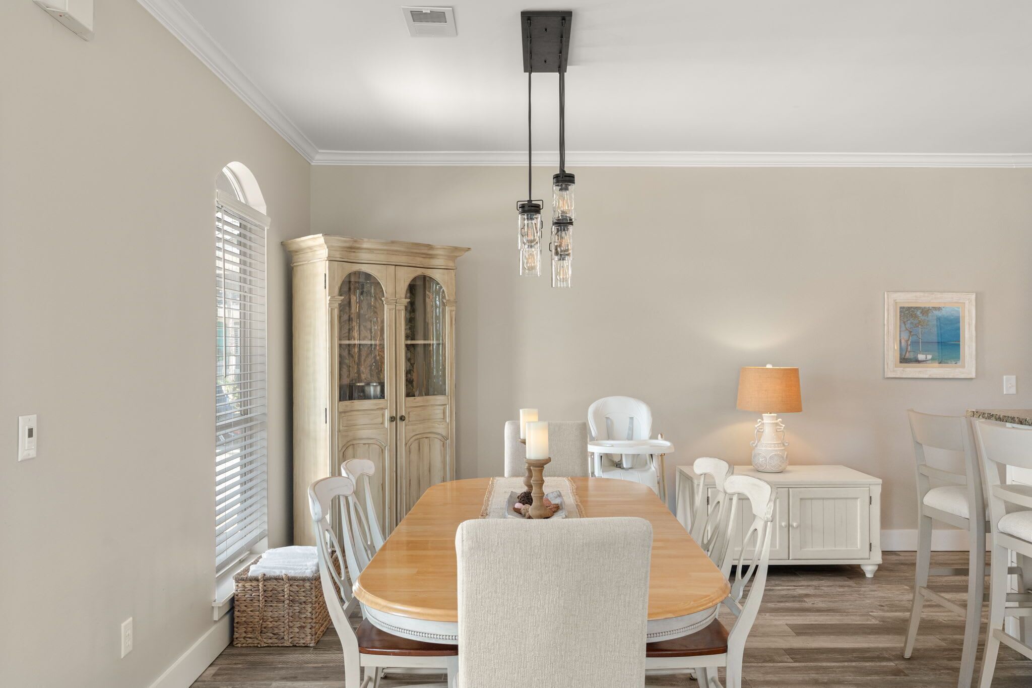 Une salle à manger avec une table en bois, des chaises blanches, un lustre et un buffet.