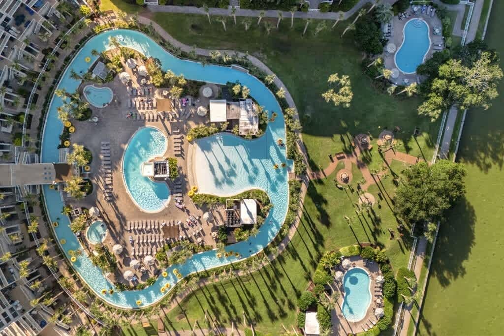 An aerial view of a resort with multiple swimming pools, sun loungers, and a well-maintained lawn area.