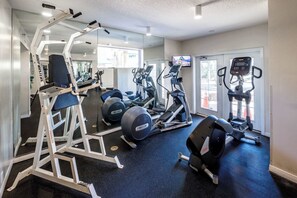 Un gimnasio con varios equipos de ejercicio, un espejo grande y una televisión.