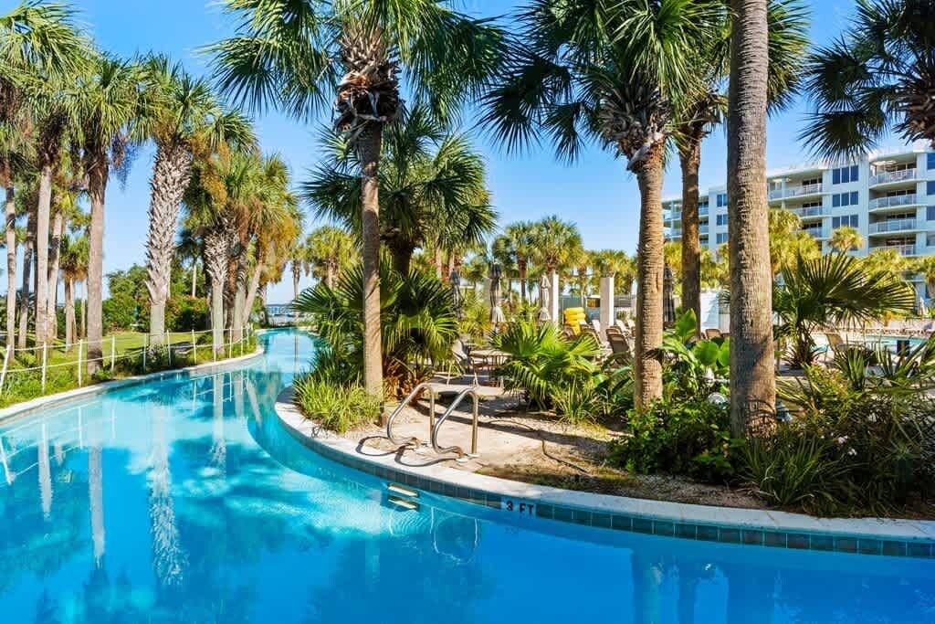 A swimming pool surrounded by palm trees and a hotel building in the background.