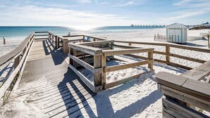 Un paseo marítimo de madera que conduce a una playa, con una pequeña estructura y un muelle al fondo.