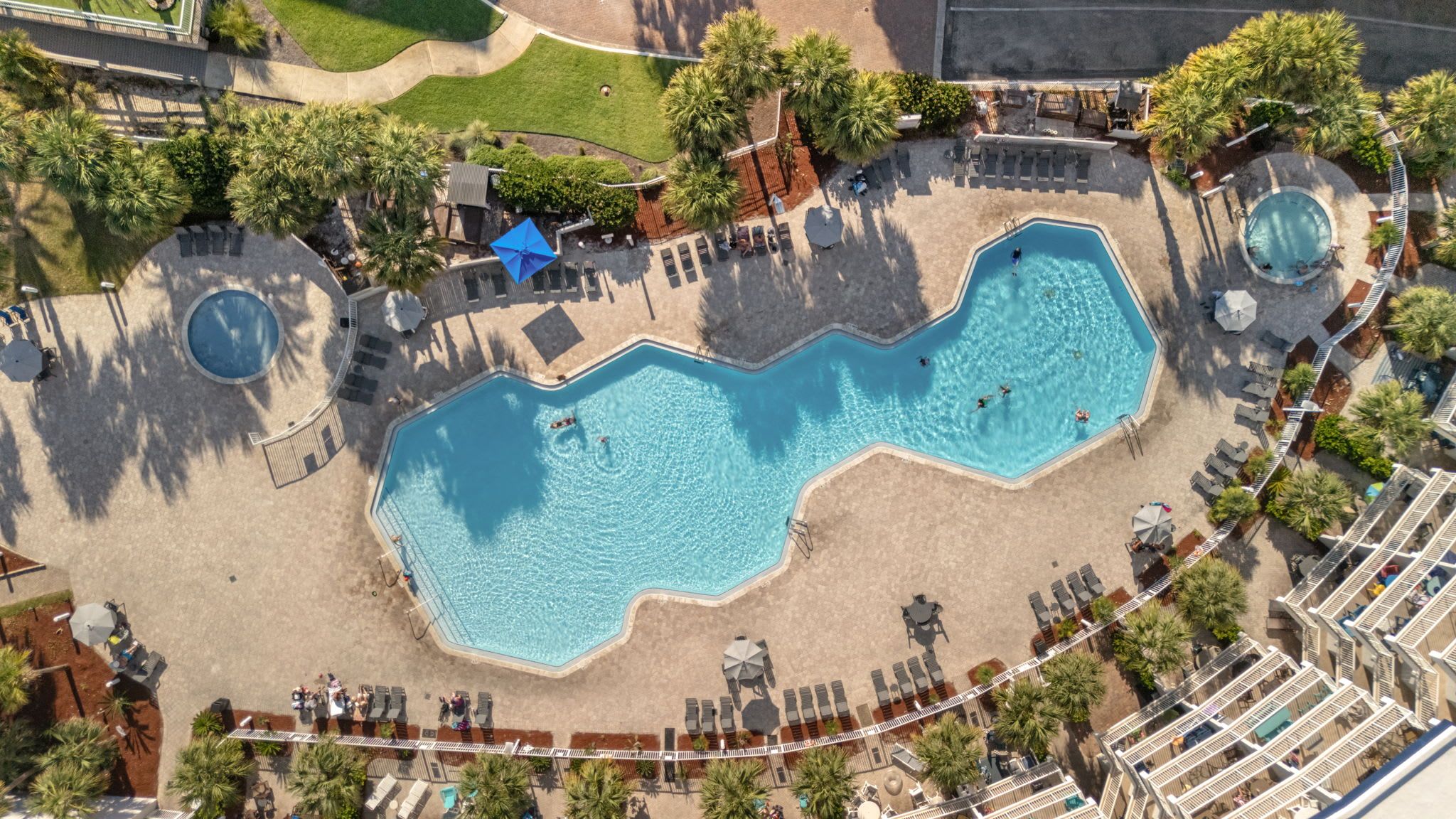 An aerial view of a resort with a large swimming pool, sun loungers, and a small circular pool.