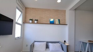 Ein Schlafzimmer mit Bett, Deckenventilator, Fernseher, Schreibtisch und einer Ziegelwand.
