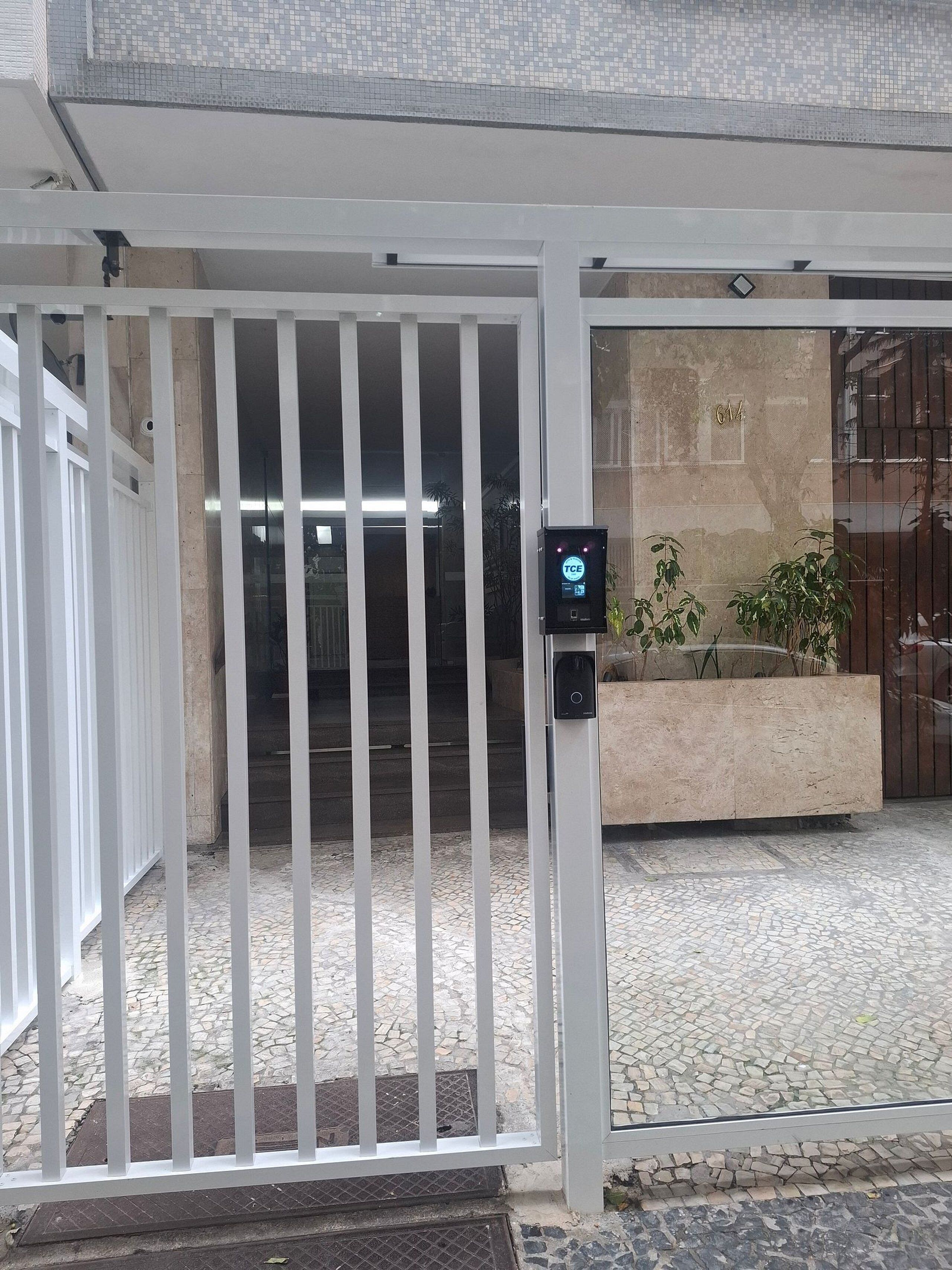 A gated entrance with a security keypad, a tiled patio, and a building facade with a tiled roof.