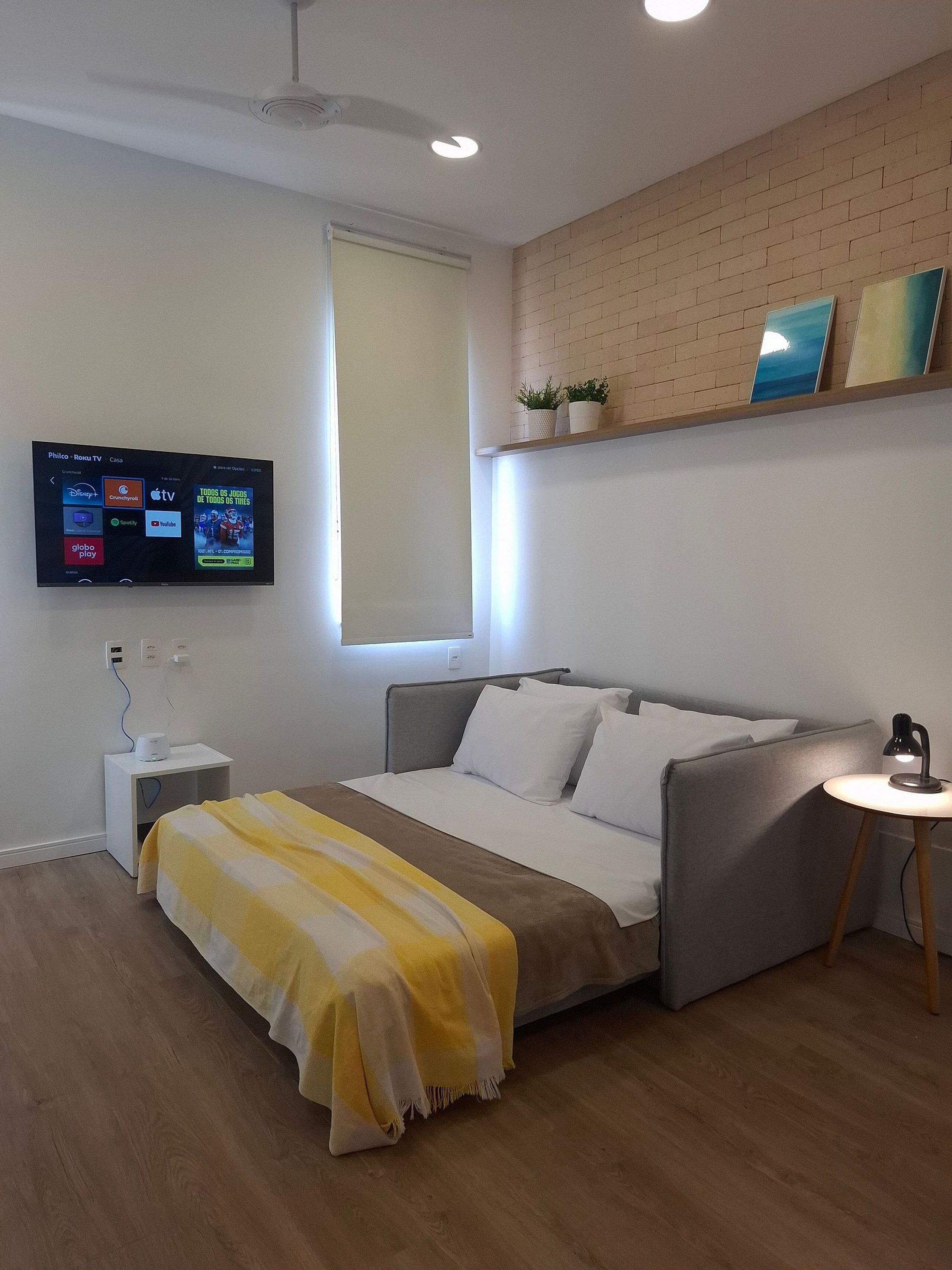 A modern bedroom with a bed, bedside table, lamp, TV, and a brick wall.