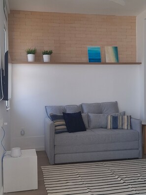 A living room with a grey sofa, a striped rug, a brick wall, and a shelf with plants and artwork. - Fullano Hosts (Rio de Janeiro)