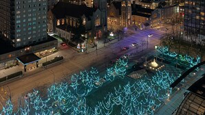 Une vue nocturne d’une ville, avec des immeubles modernes de grande hauteur, une rue bien éclairée et des illuminations décoratives.