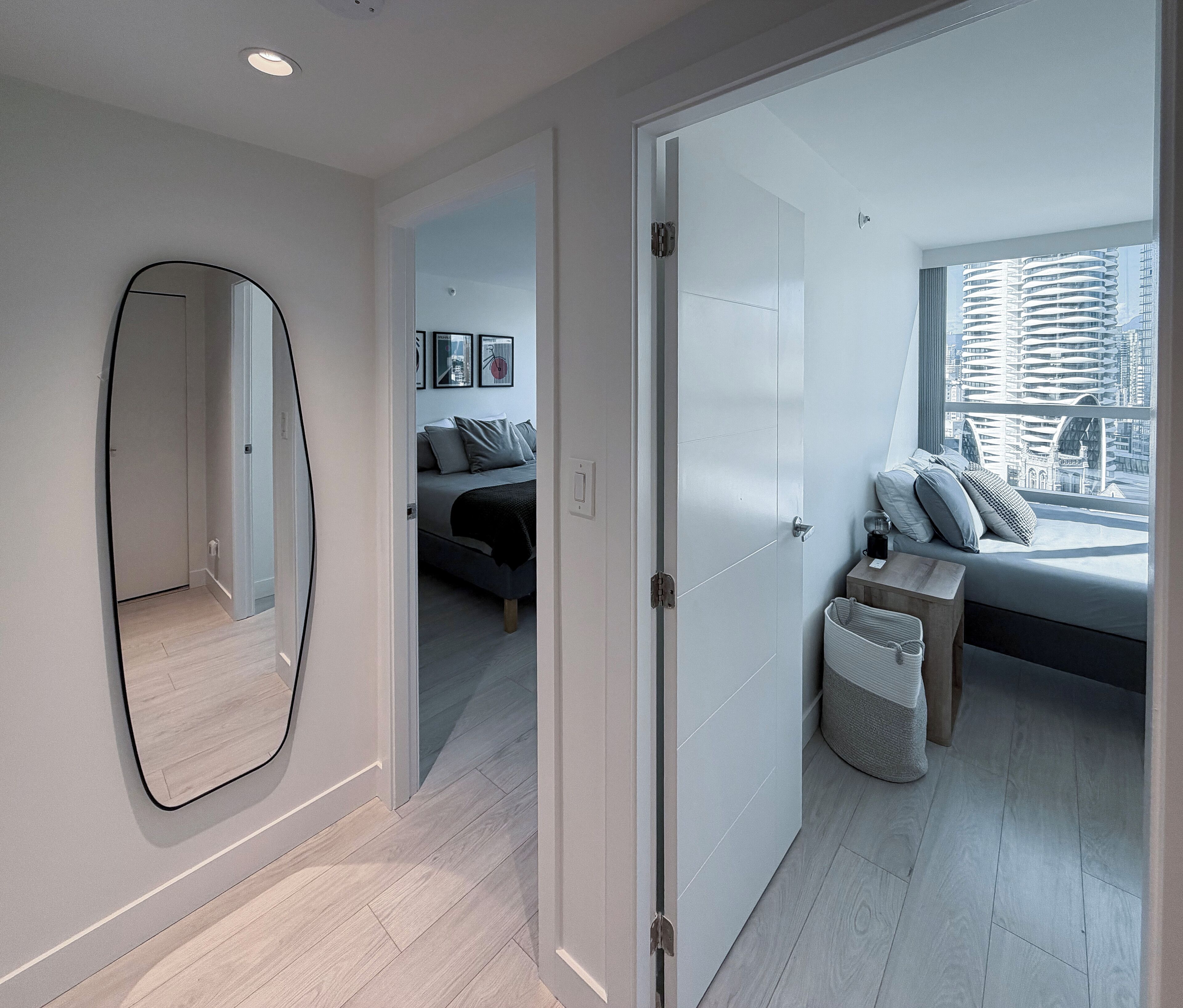 Une chambre moderne avec un grand lit, un coin salon avec vue et un couloir agrémenté d’un miroir.