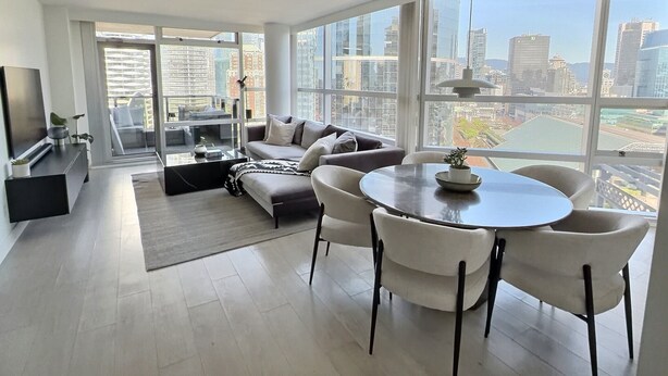 Un salon moderne comprenant un canapé, une table à manger et des chaises, de grandes fenêtres offrant une vue sur la ville et un téléviseur à écran plat.