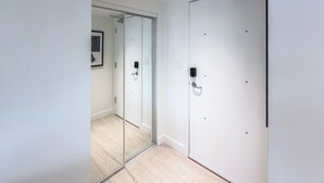 Un couloir avec une porte en verre, un mur blanc et un interrupteur.
