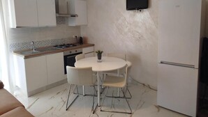 Eine kompakte Küche mit weißen Schränken, einem runden Tisch mit Stühlen, einem eingebauten Backofen und einem an der Wand montierten Fernseher.