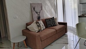 Ein Wohnzimmer mit einem braunen Sofa, einem kleinen Beistelltisch und einem Bild eines Rehs an der Wand.