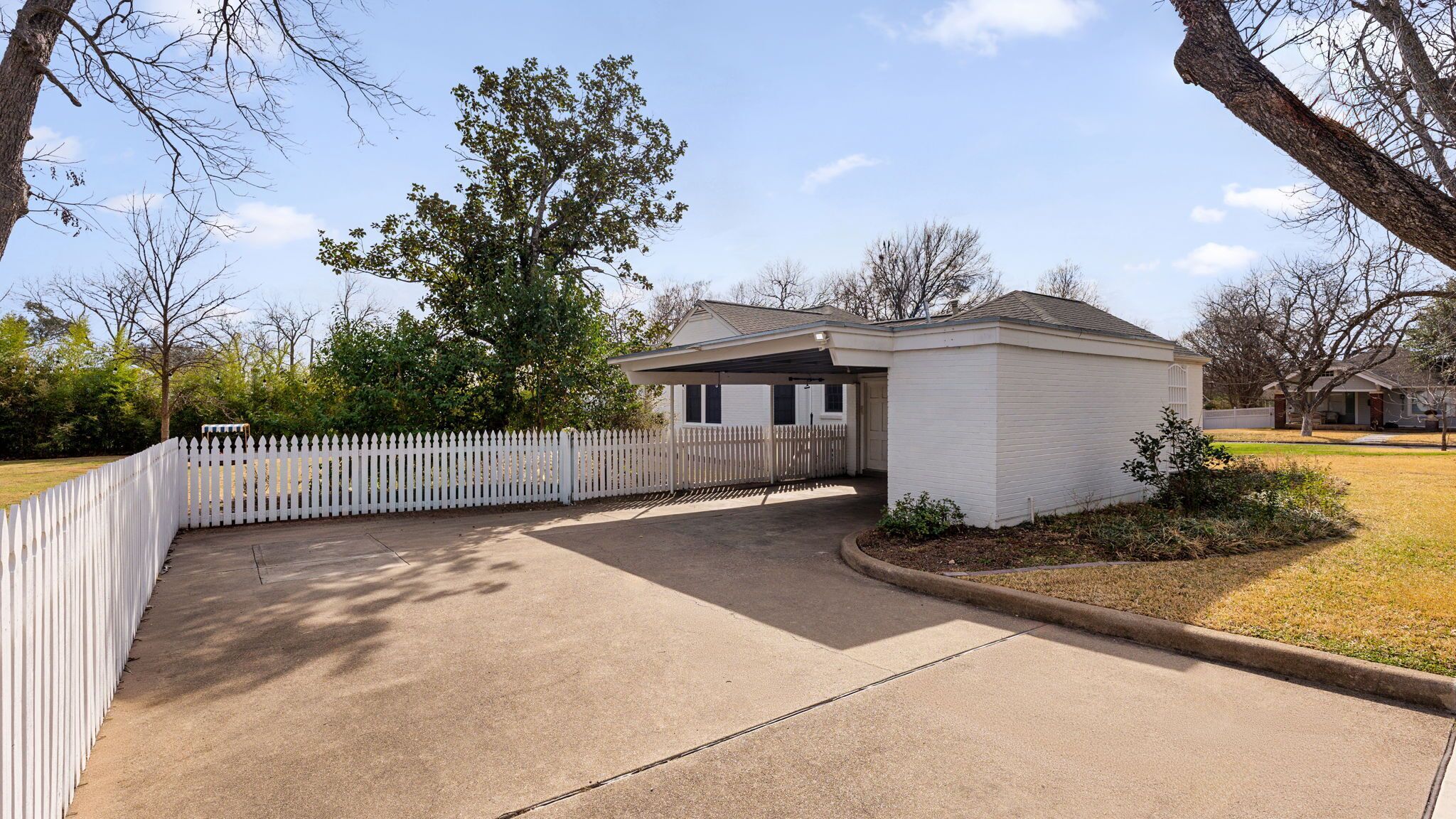 A single-story house with a covered porch, a fenced yard, and a clear sky.