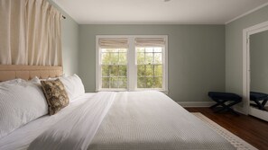 A bedroom with a large bed, two windows with curtains, a bedside table, and a chair. - Olive St (Georgetown)