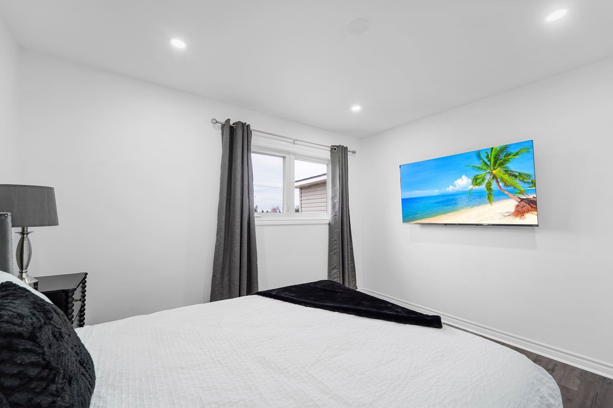 Ein Schlafzimmer mit Bett, einem Vorhangfenster, einem Strandbild und einer Lampe.