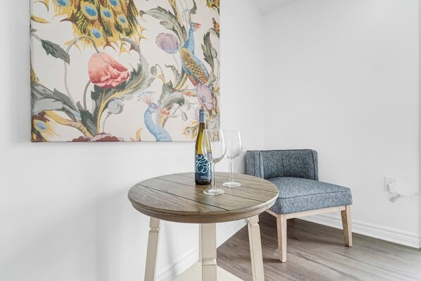 A room with a round wooden table, a blue armchair, and a large floral painting on the wall. - Our stylish, comfy home in wine country blends relaxation & convenience. (Niagara-on-the-Lake)