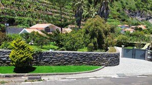 A residential area with houses, a stone wall, and a paved driveway. - Villa Atlântico Garden Apartment (Arco da Calheta)
