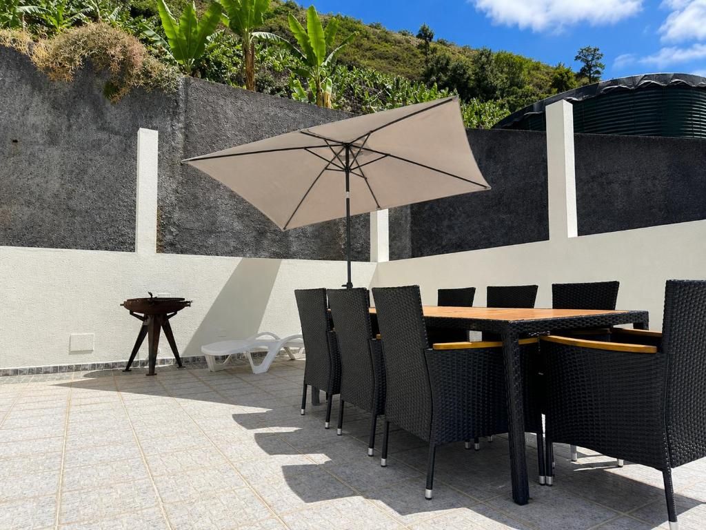 Un patio al aire libre con una mesa y sillas, un paraguas grande y una pequeña mesa con un taburete.