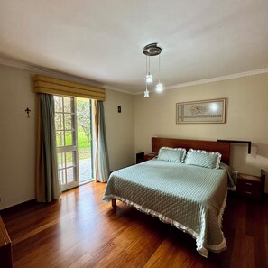 Ein Schlafzimmer mit einem großen Bett, einem Nachttisch, einer Lampe, einer Deckenleuchte und einem Fenster mit Vorhängen.