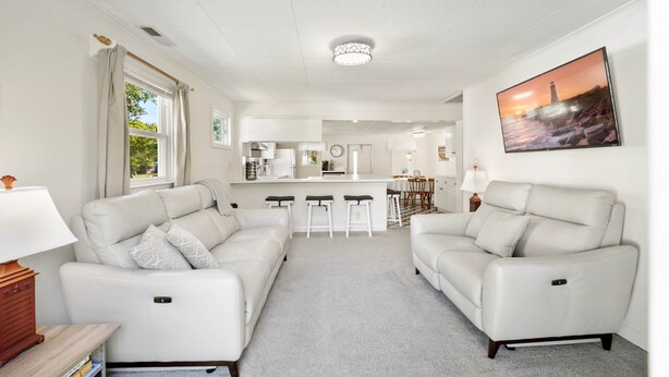 Ein modernes Wohnzimmer mit zwei weißen Ledersofas, einem Küchenbereich im Hintergrund und einem großen Flachbildfernseher an der Wand.