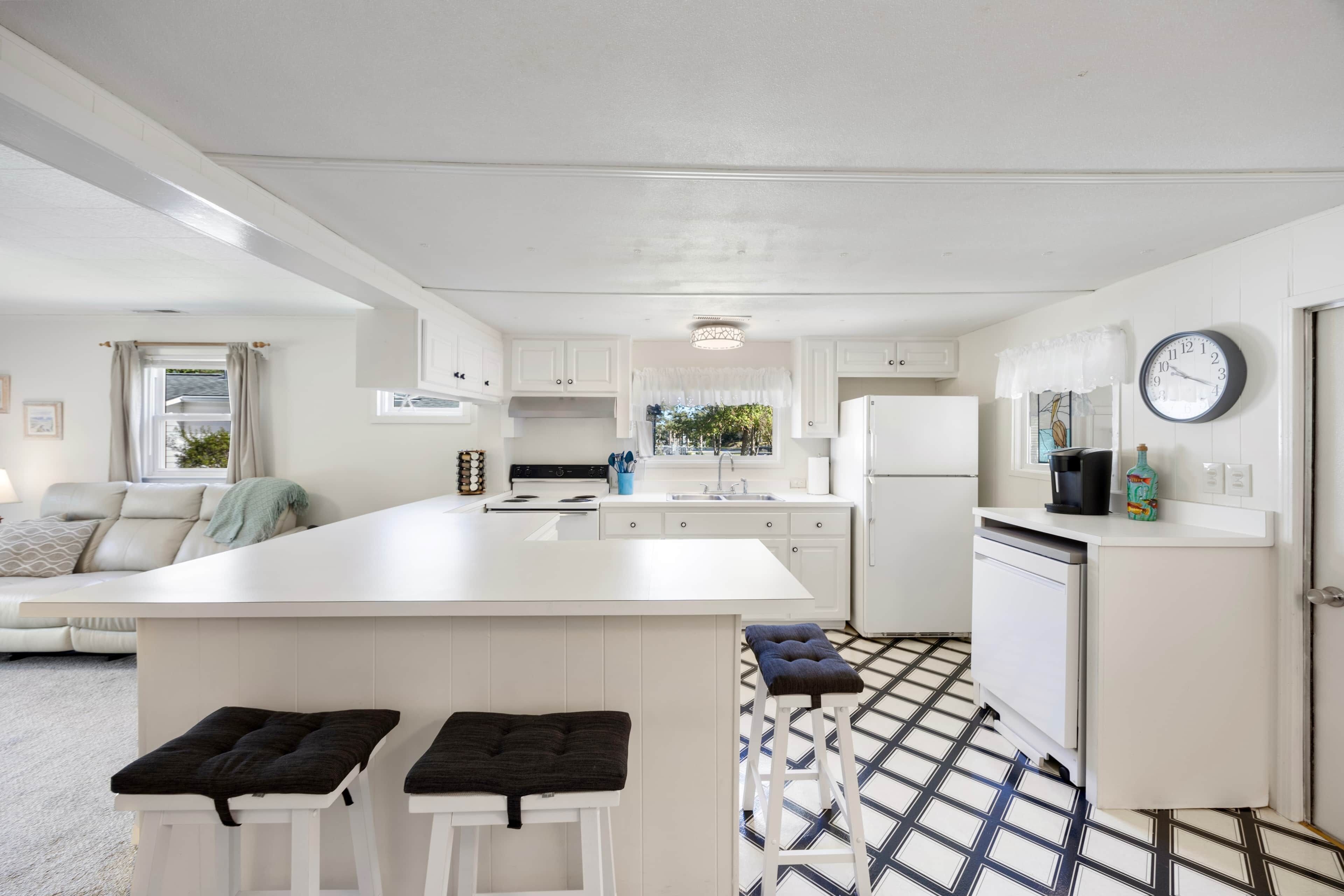 A modern kitchen with white cabinetry, a central island, and a dining area with two stools.