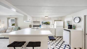 A modern kitchen with white cabinetry, a central island, and a dining area with two stools.