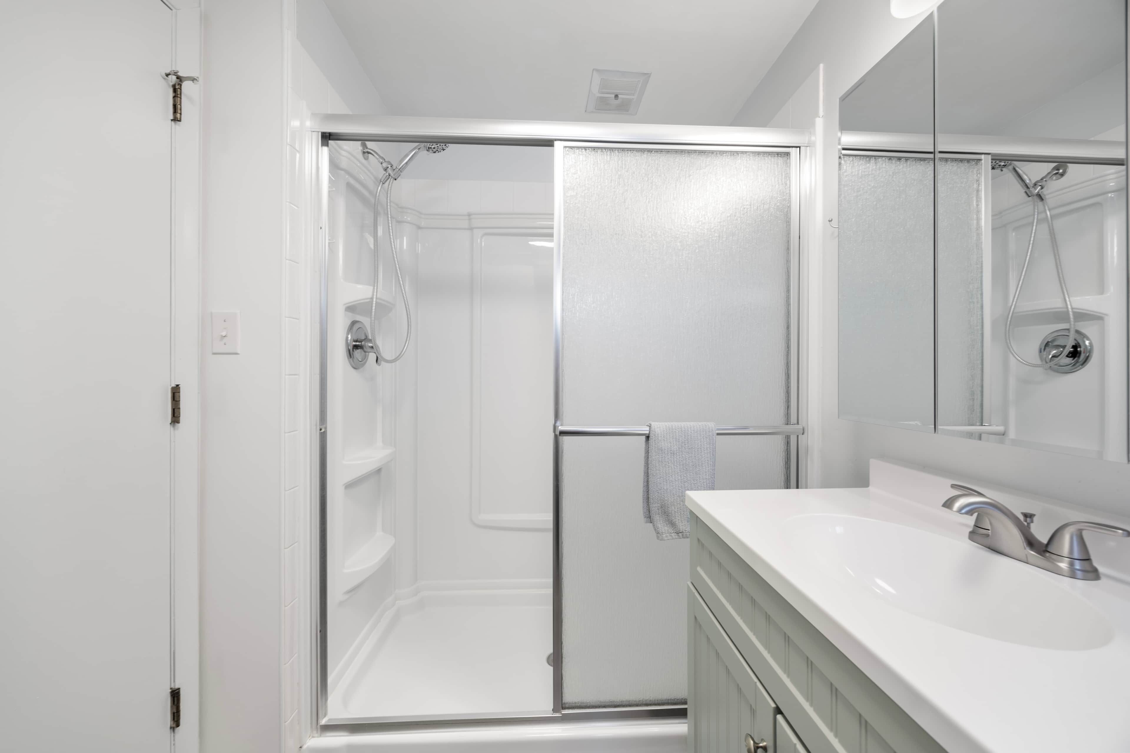 A modern bathroom with a glass shower enclosure, a white sink with a single faucet, and a large mirror.