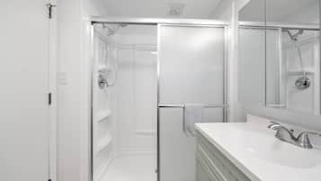 A modern bathroom with a glass shower enclosure, a white sink with a single faucet, and a large mirror.