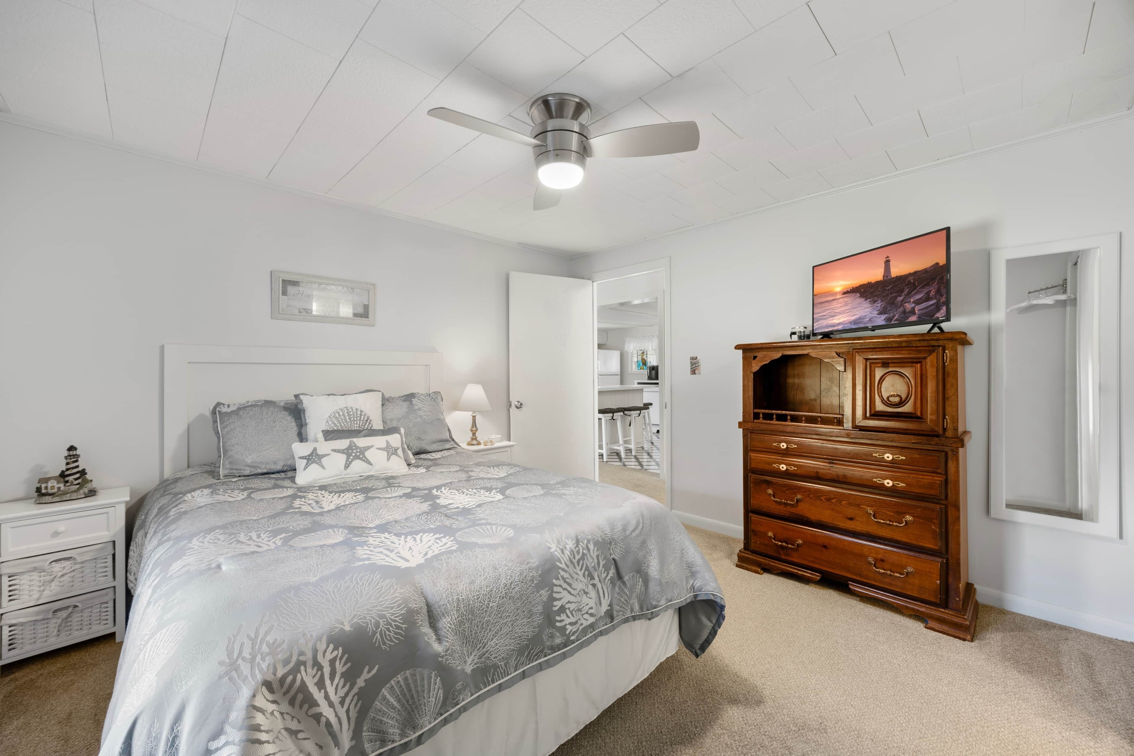 Quarto com cama, penteadeira, ventoinha no teto, televisão e mesa de cabeceira.