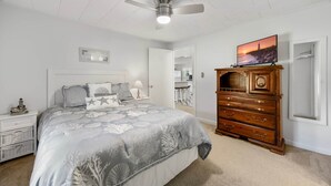 Ein Schlafzimmer mit einem Bett, einem Schminktisch, einem Deckenventilator, einem Fernseher und einem Nachttisch.