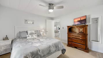 Quarto com cama, penteadeira, ventoinha no teto, televisão e mesa de cabeceira.