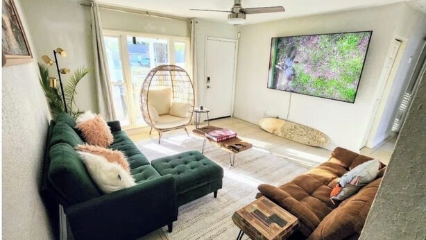 A living room with a green sofa, a brown sofa, a wooden coffee table, a wicker chair, and a television on the wall. - 3-bedroom house in amazing Orlando with AC and fitness room-BEACH STYLE BUNGALOW (Orlando)