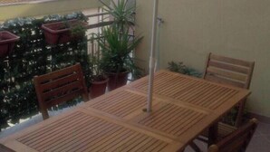 Una mesa de madera con un paraguas amarillo, dos sillas, plantas en macetas y vista a un paisaje urbano.