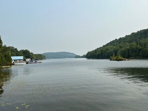 A calm river with boats, a dock, and a forested hill in the background.