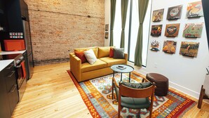 Un salon chaleureux avec un mur en briques, un canapé jaune, une petite table ronde et un tapis à motifs.