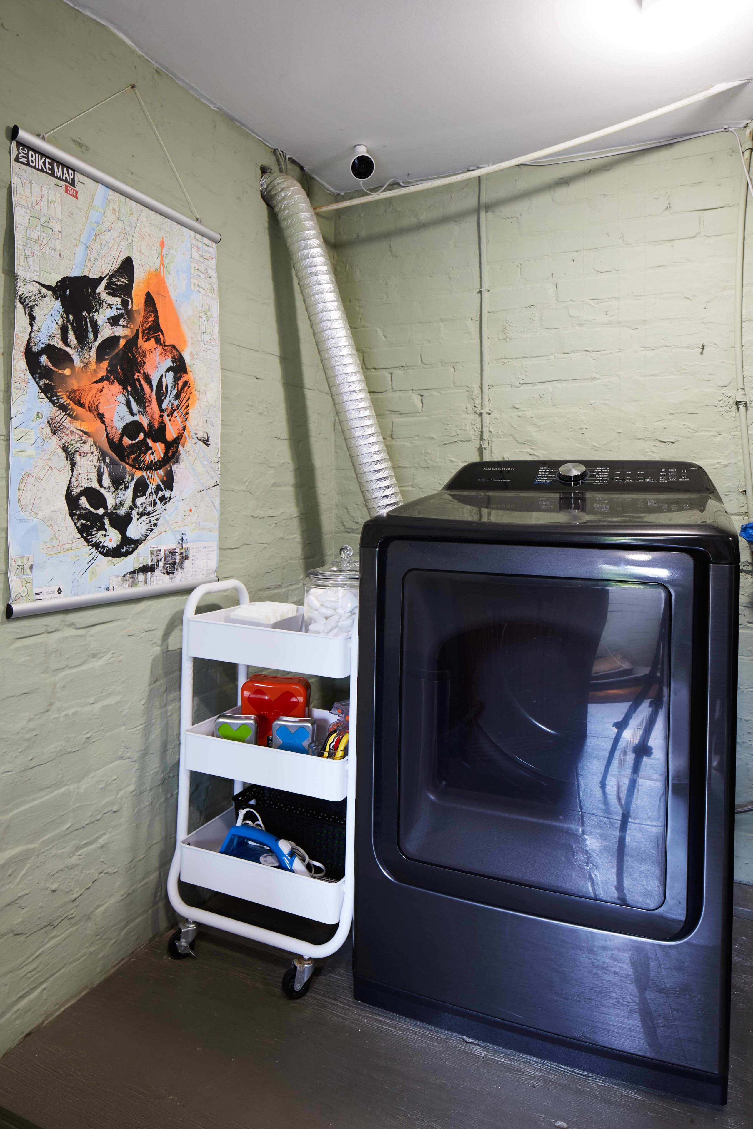 Una habitación con un mapa colgado en la pared, un carrito con diversos objetos y un electrodoméstico negro.
