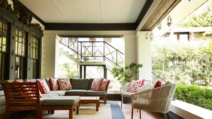 A cozy indoor seating area with a sofa, chairs, and a coffee table, featuring a staircase and greenery outside. - Apt2@EdenBrae - Walkable Southern Gothic Mansion (Birmingham)