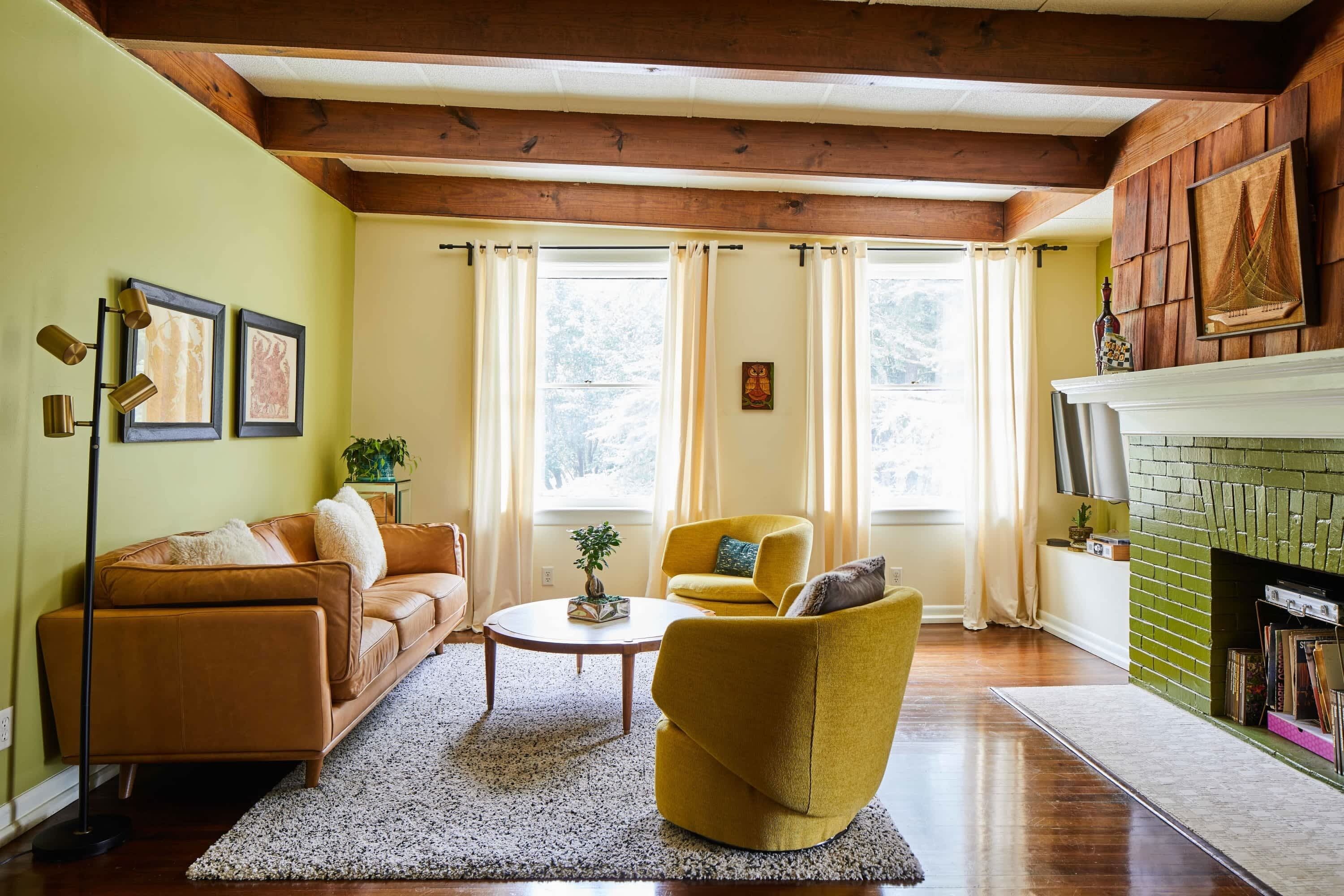Un salon comprenant un canapé, un fauteuil et une table basse, une cheminée et une fenêtre avec des rideaux.