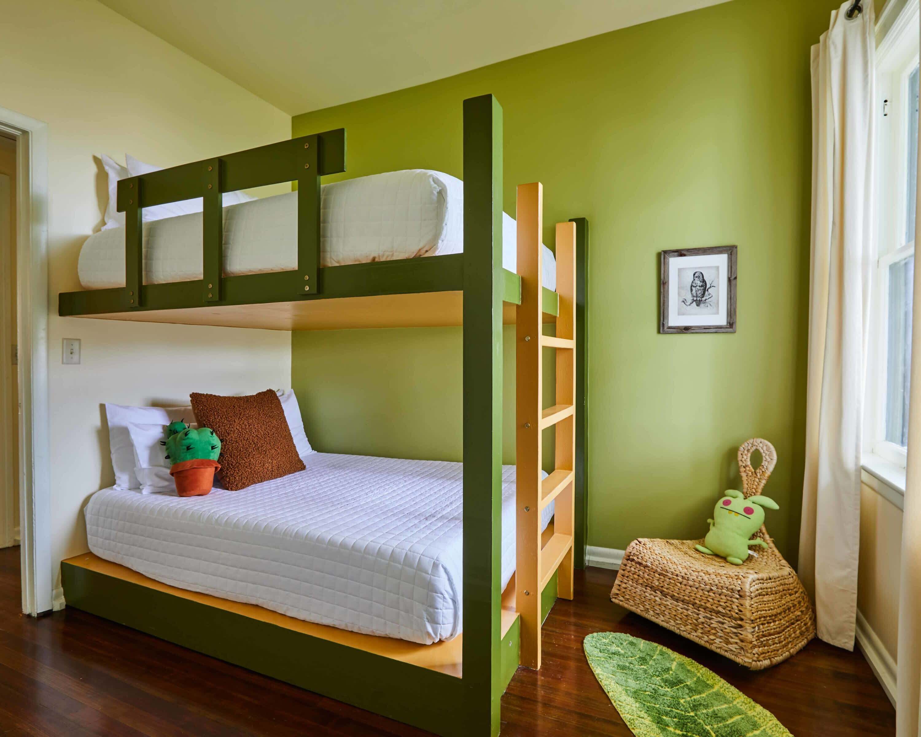 Une chambre avec un lit superposé, un mur vert, un tableau encadré et un petit tapis vert.