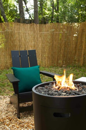 Ein Garten mit Feuerstelle, einem Holzstuhl mit grüner Sitzkissen und einem Bambuszaun.