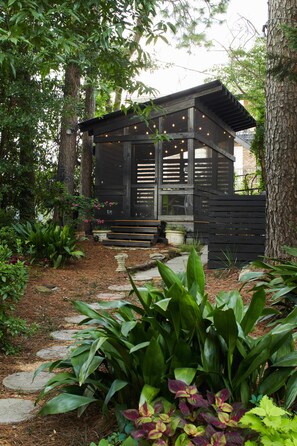 Una cabaña de madera con un porche, rodeada de árboles y plantas.