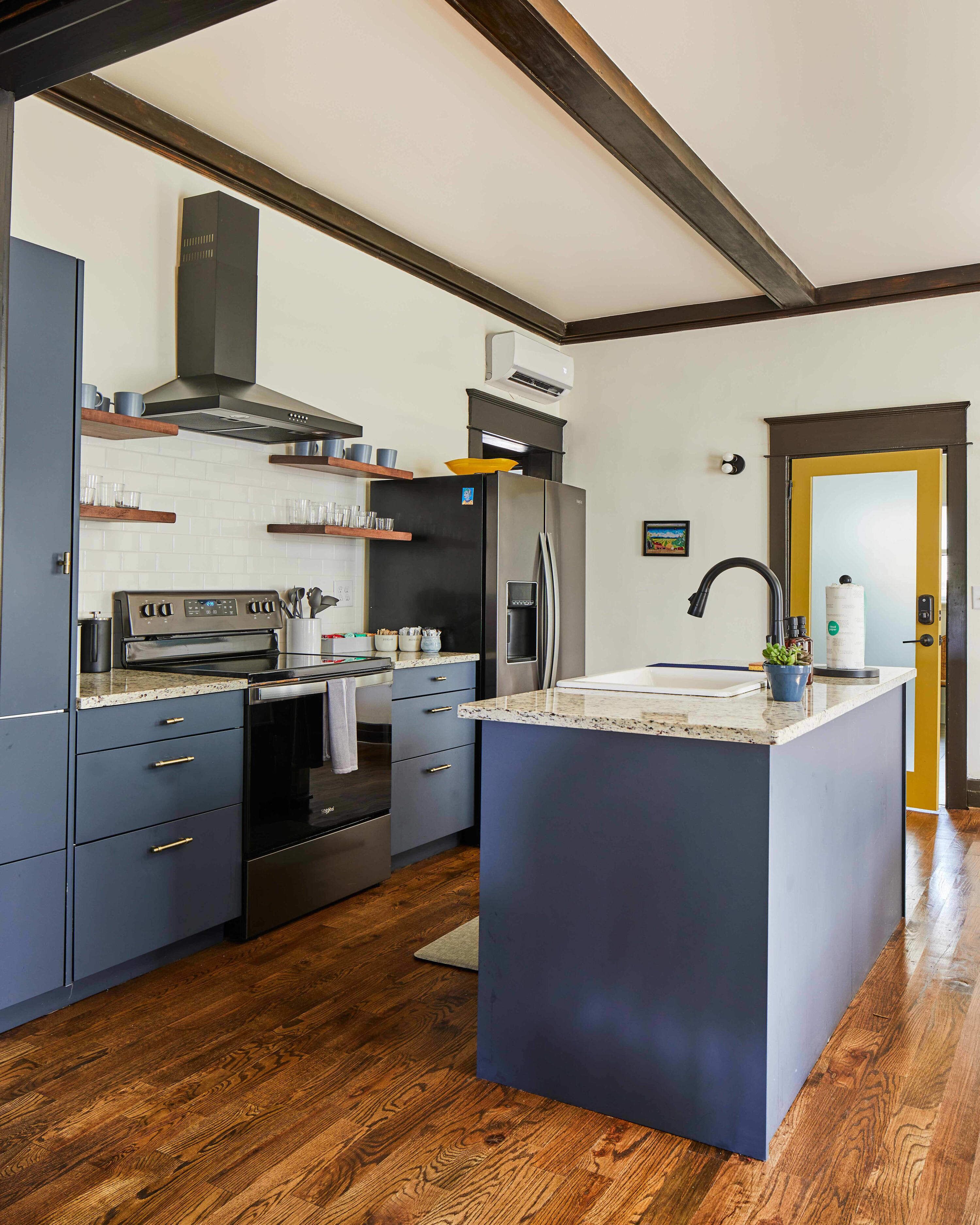 A modern kitchen with a central island, built-in oven, stainless steel appliances, wooden flooring, and a dark blue cabinetry.