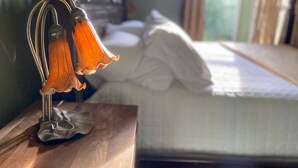 A bed with white bedding, a wooden bedside table with a lamp, and a window with curtains. - Victorian on Garden: Best Location in Town (Bellingham)