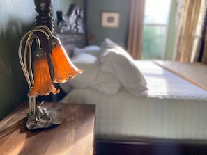 Un lit avec une literie blanche, une table de chevet en bois avec une lampe, et une fenêtre avec des rideaux.