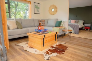 A living room with a sofa, a wooden coffee table, a cowhide rug, a bed, and a small side table.