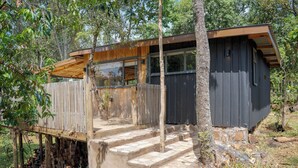 A wooden cabin with a deck, surrounded by trees.