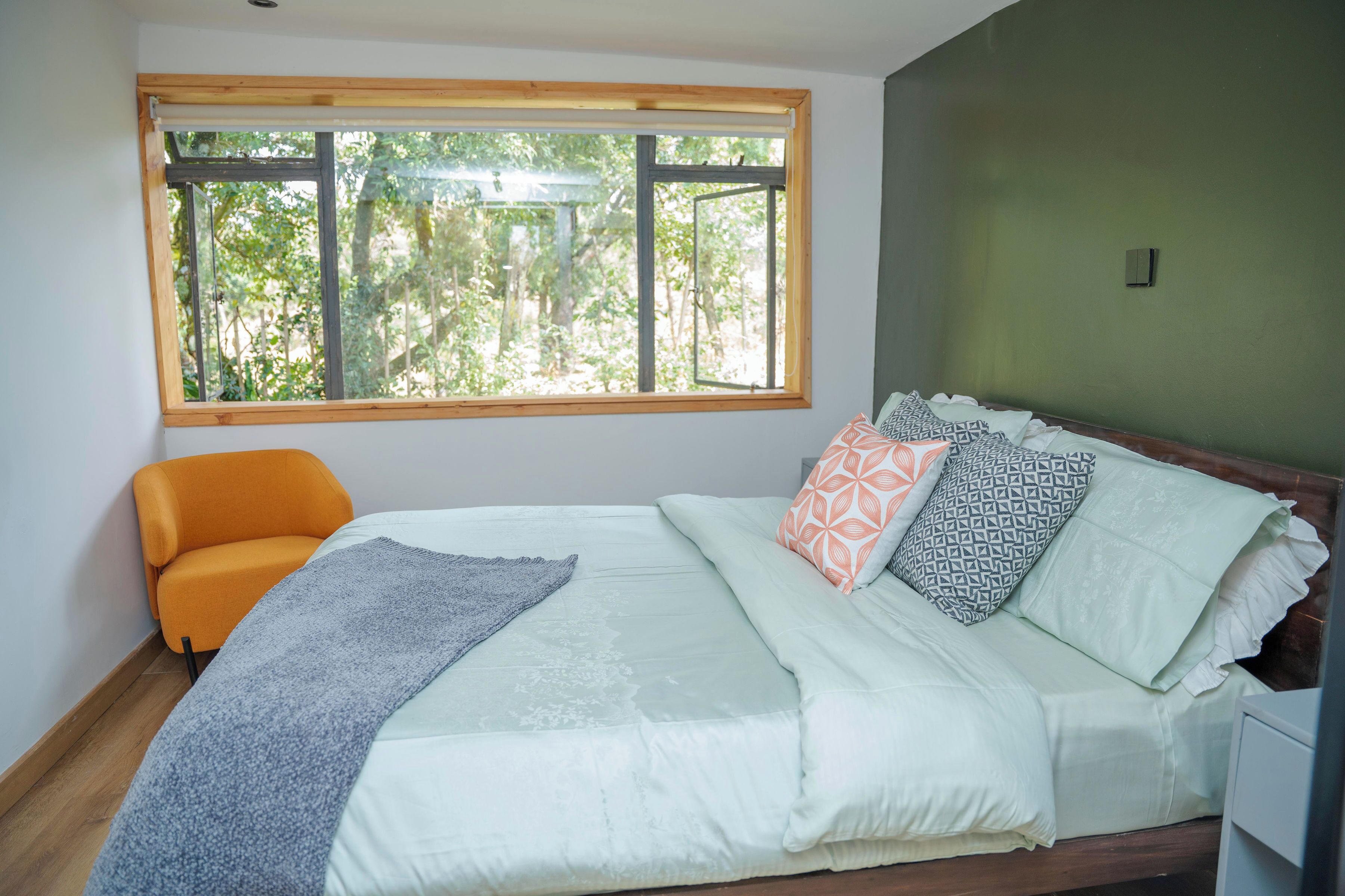 Un dormitorio con cama, ventana, silla y mesita de noche.